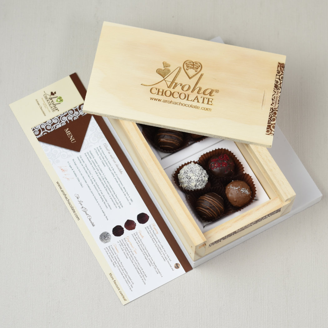Aroha Chocolate Eight Mixed Truffles Luxury Wooden Gift Box. There is an open wooden gift box displaying the beautiful hand rolled chocolate truffles within. The sliding lid with the Aroha Chocolate brand sits on top of the open box. Below is the included flavour chart menu.